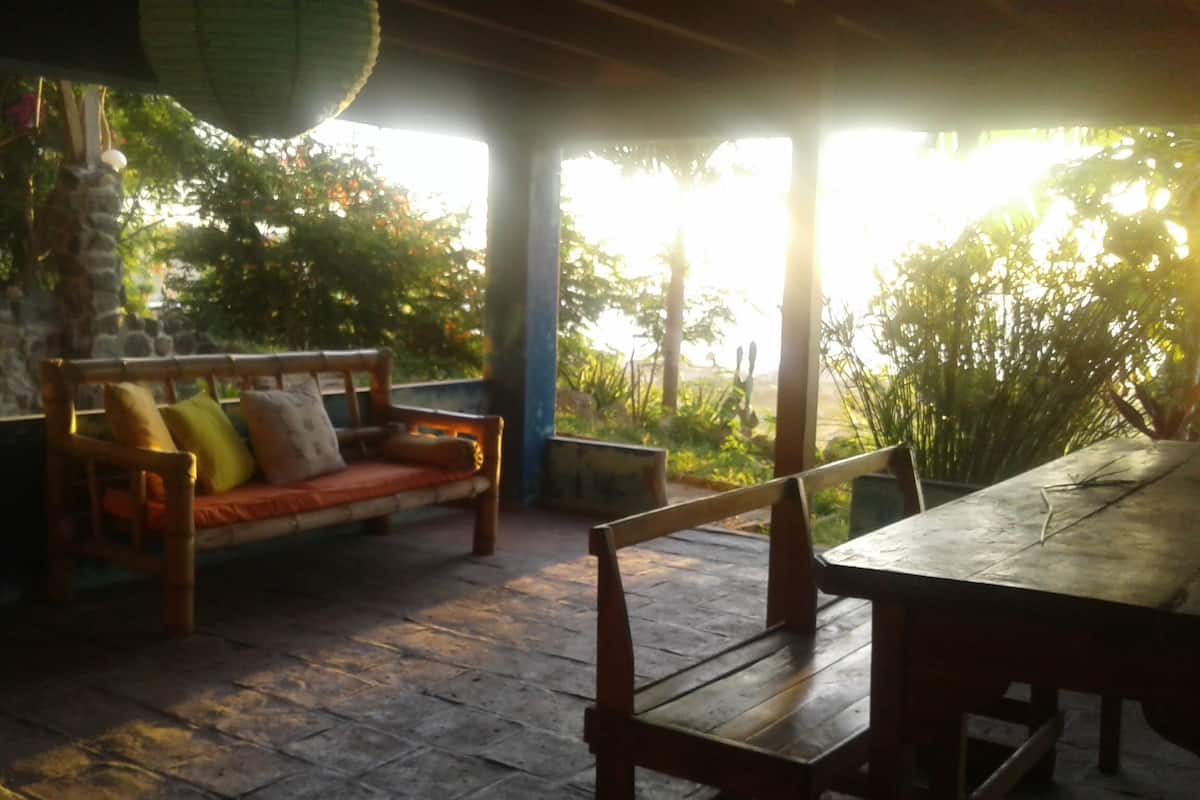 A wooden bench and table under a covered area with stone walls and a view of greenery.