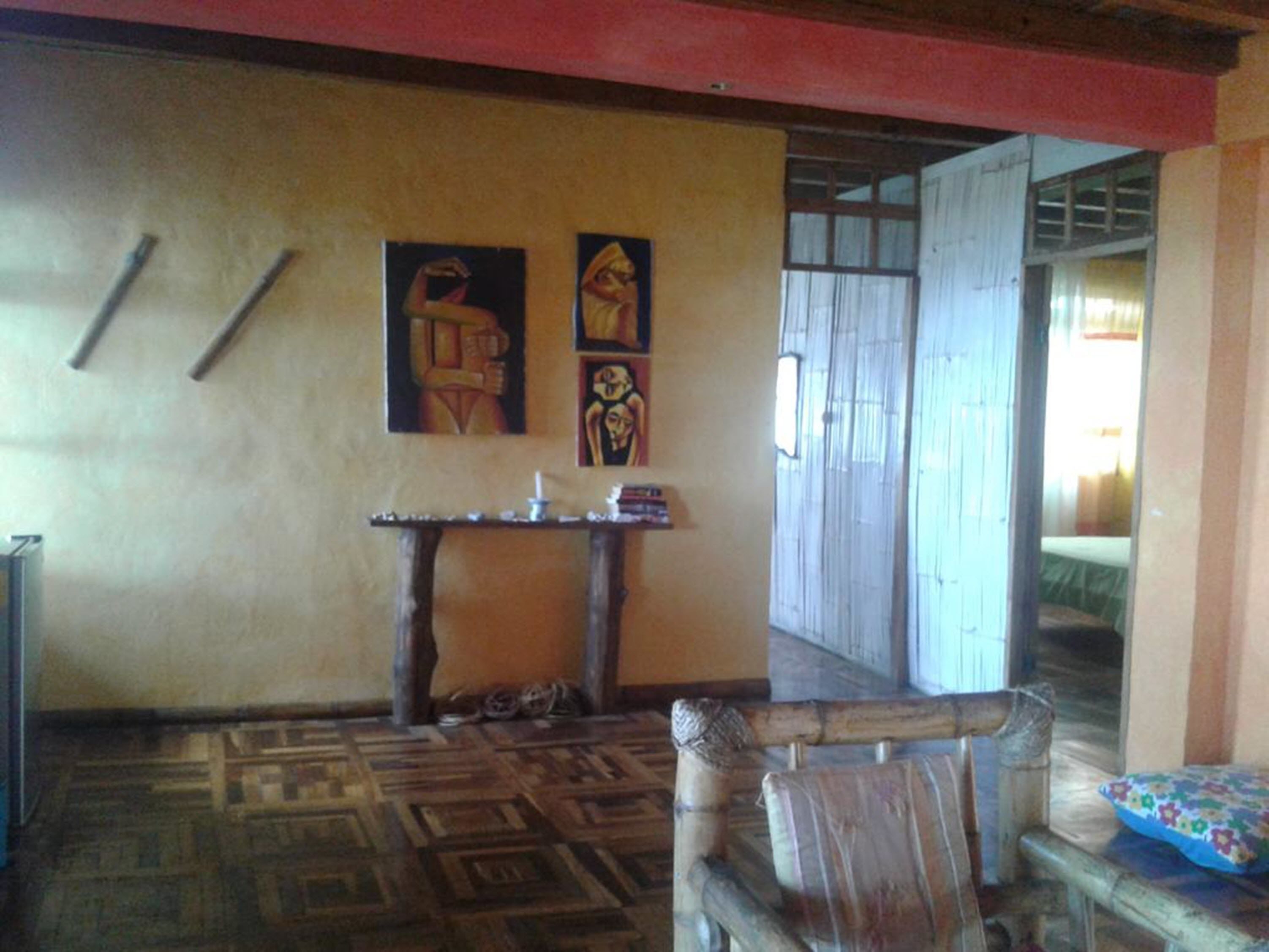 A room with a patterned floor, a wooden chair, a small table with a candle, and two paintings on the wall.
