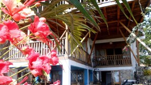 Un bâtiment à deux étages doté d’un balcon, d’un toit en bois et d’un jardin agrémenté de plantes et de fleurs.