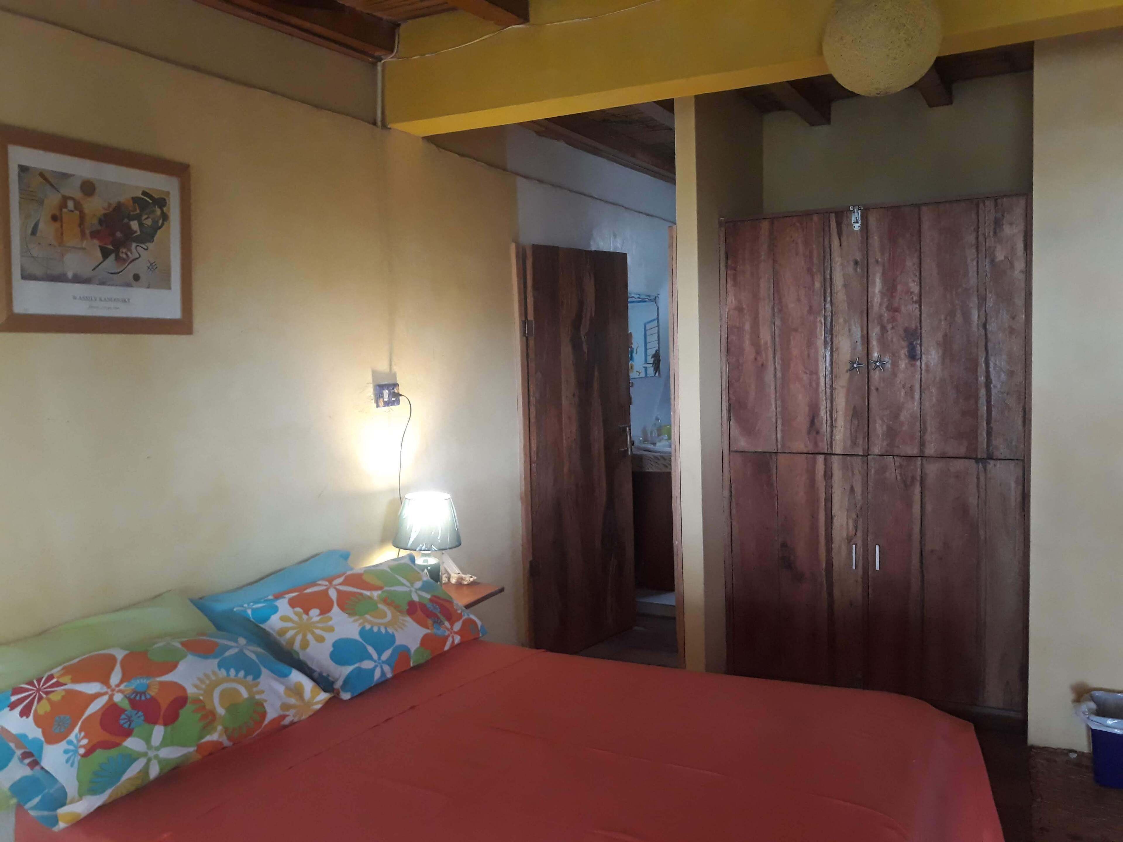 Un dormitorio con una cama, un armario de madera, una lámpara de pared y un cuadro enmarcado.