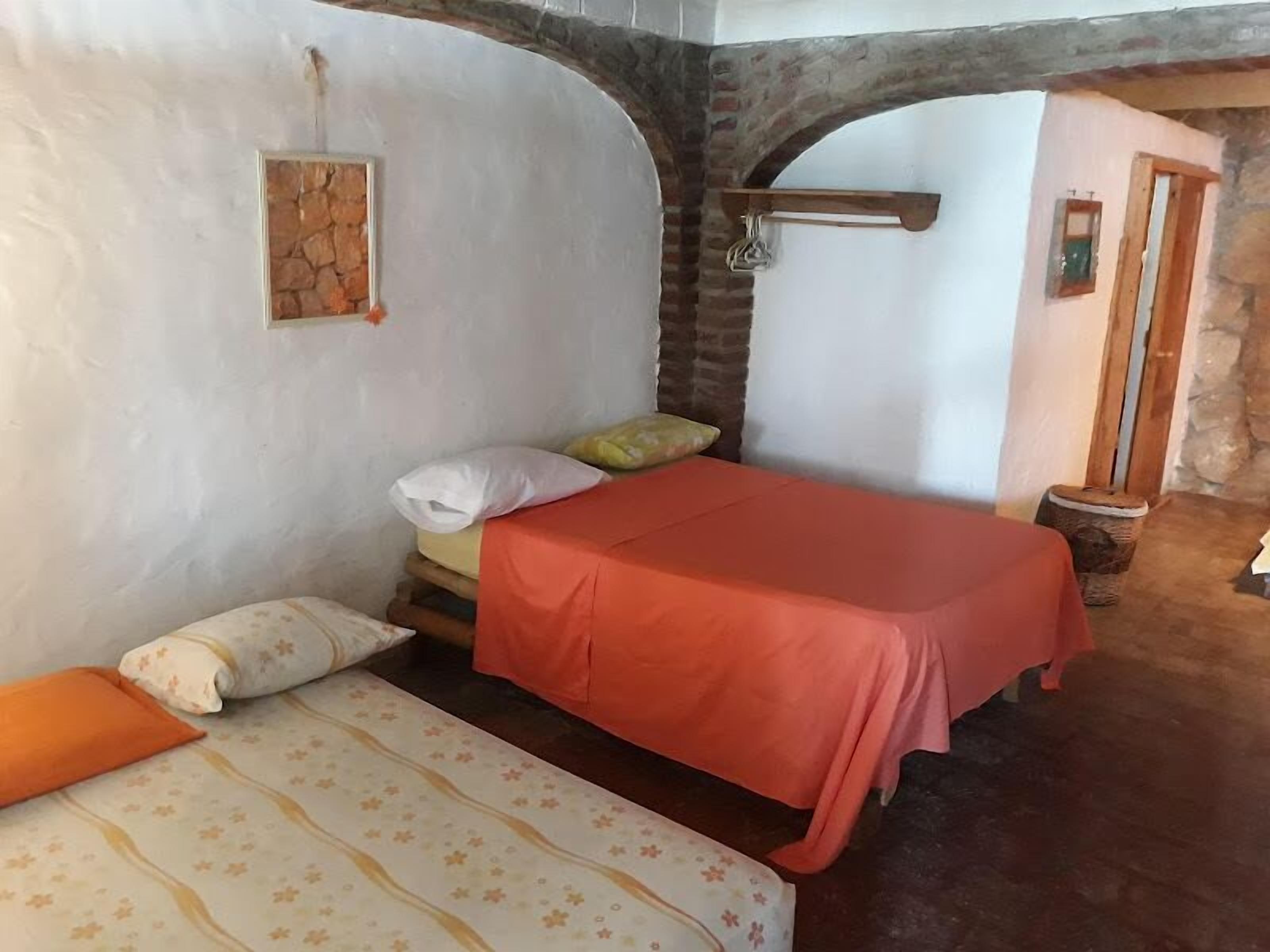 A bedroom with a bed, pillows, a wooden bench, a stone wall, and a small window.
