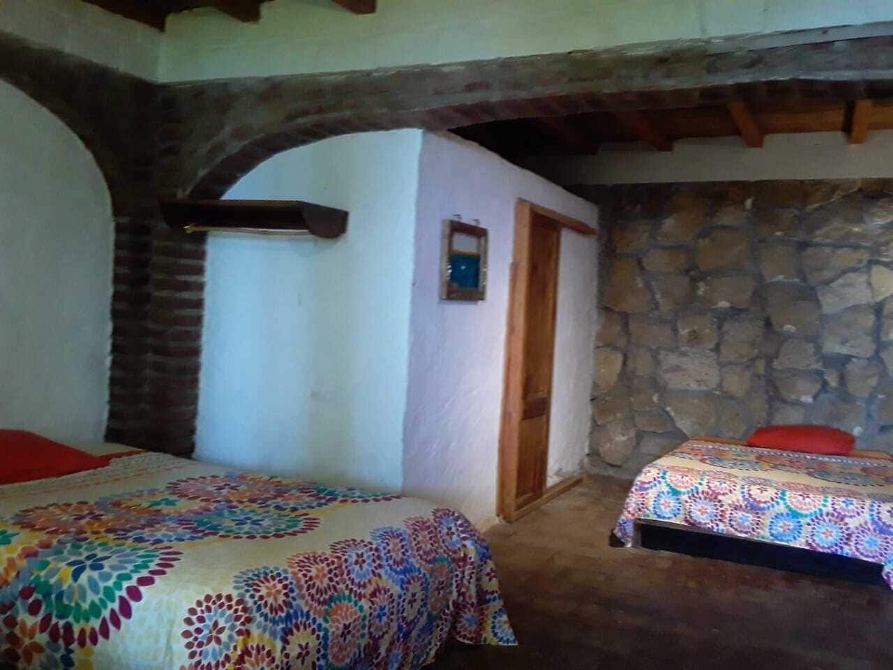 A room with two beds, each with a colorful patterned bedspread. There is a stone wall and a wooden door in the room.