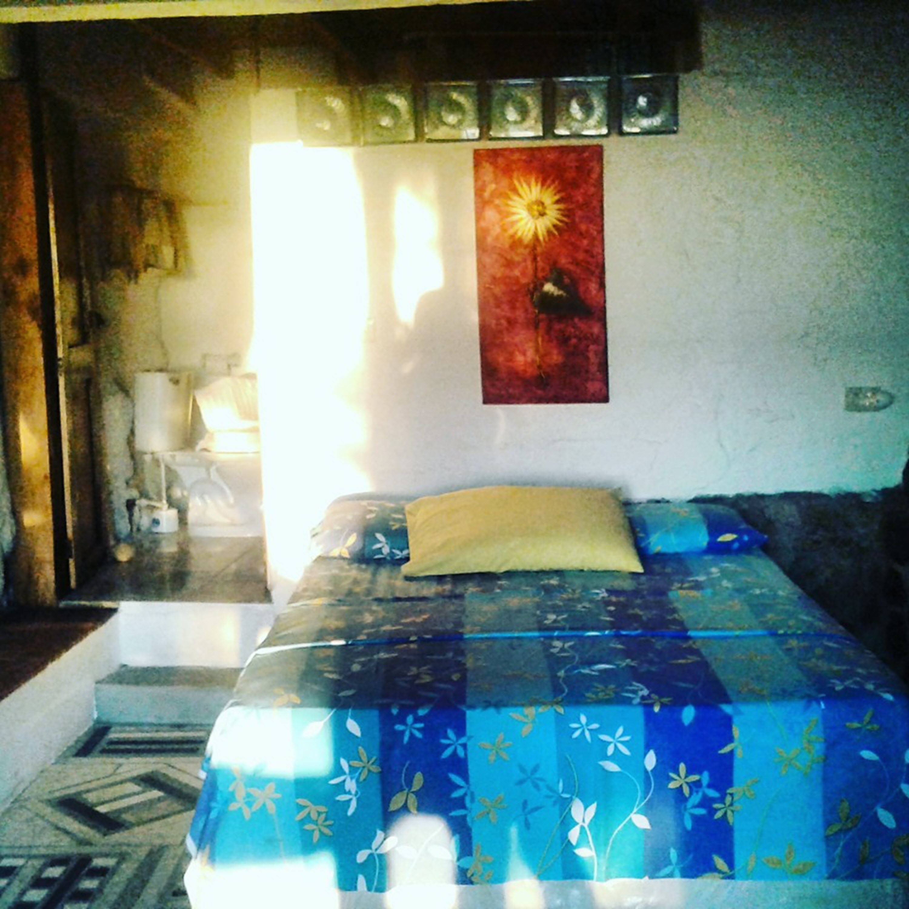 Un dormitorio con una cama, una mesita de noche, una lámpara y una pared decorada con marcos.