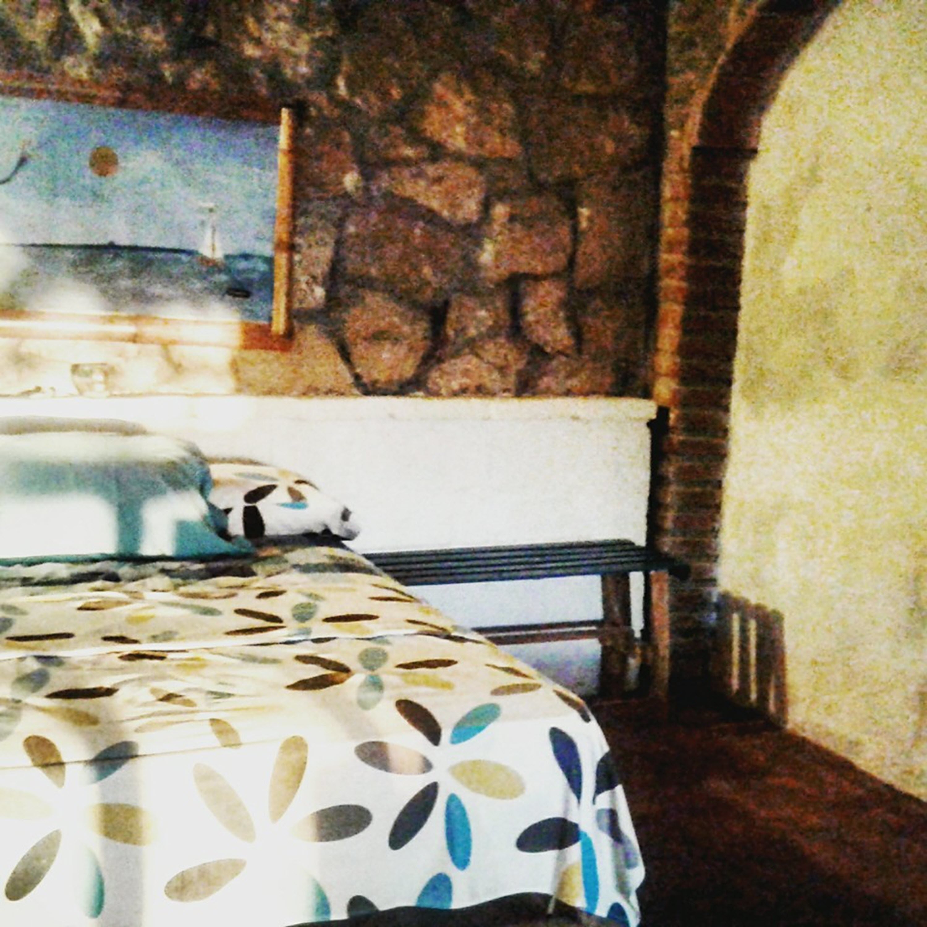 A room with a bed, a stone wall, and a window with a view of a building.