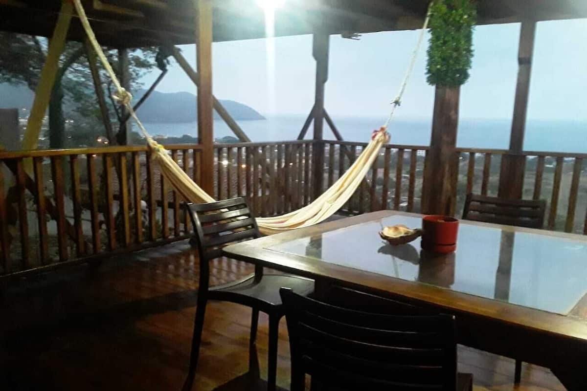 A wooden deck with a glass table and chairs, a hammock, and a view of the sea.