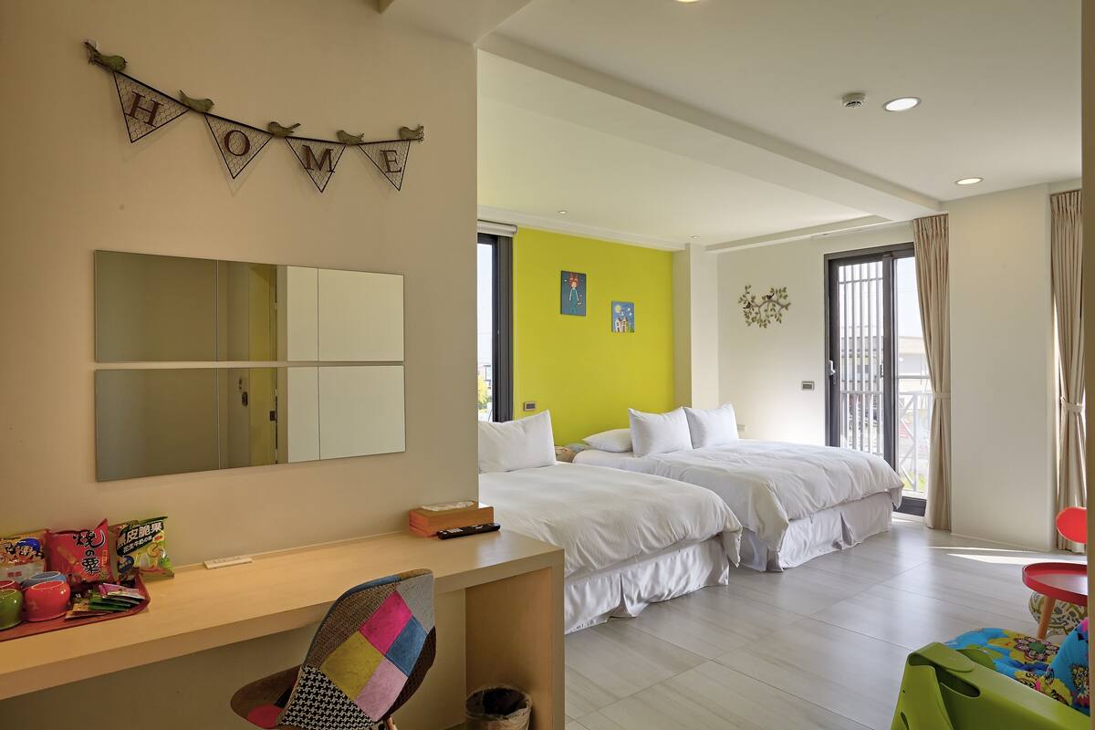 Quarto de hotel com uma cama grande, uma escrivaninha com cadeira, um espelho e uma janela com cortinas.