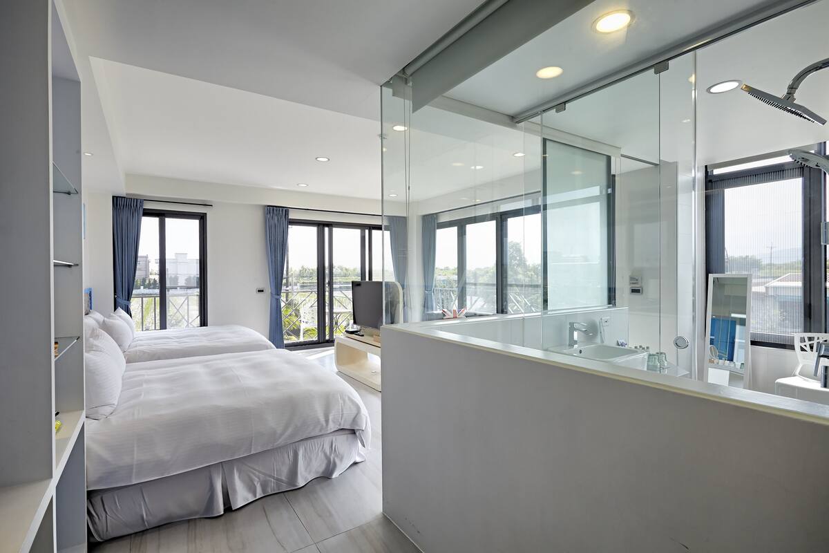 Quarto de hotel moderno com uma cama grande, uma televisão, banheiro com um espelho amplo e varanda com vista.