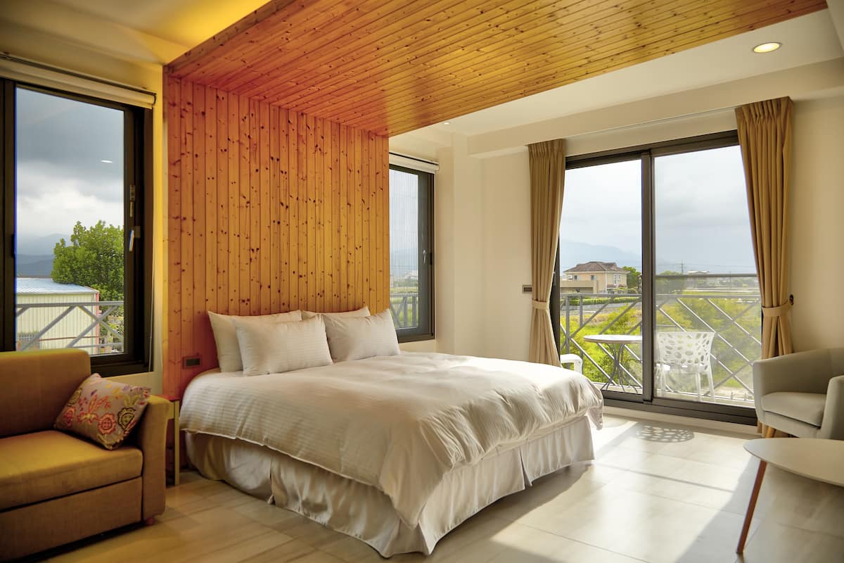 Quarto com cama grande, teto de madeira, varanda e vista, além de um sofá.