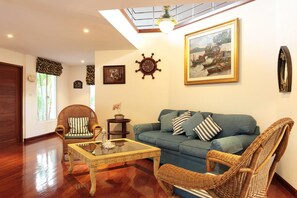 A living room with a blue sofa, wicker chairs, a glass coffee table, and a painting on the wall. - Prompimarn Villa (Pranburi)
