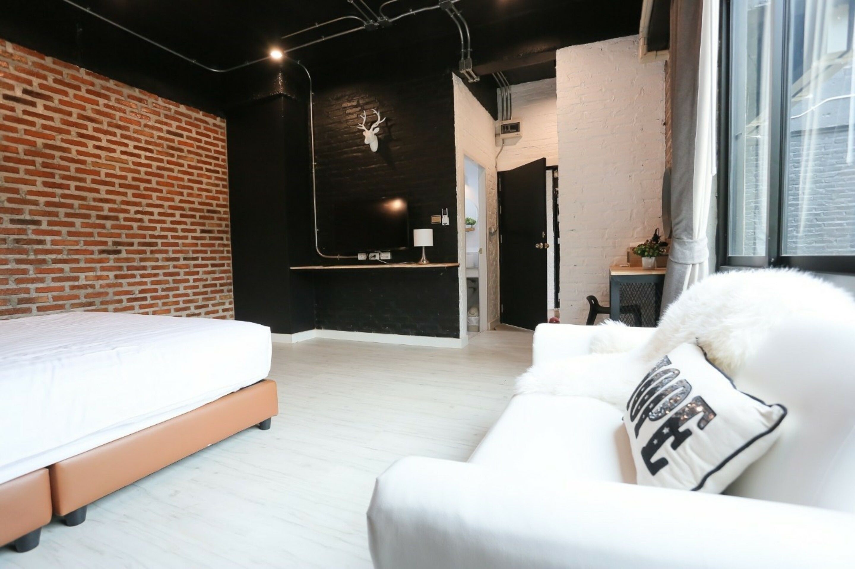 A modern bedroom with a brick wall, a bed, a white sofa, and a mounted deer head.