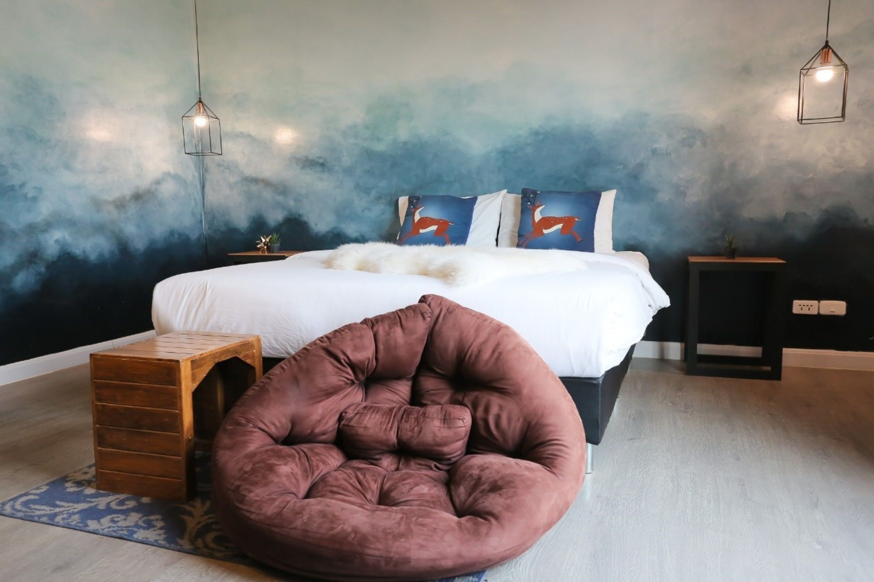 Une chambre à coucher avec un lit, un tabouret en bois, un pouf et une table de chevet.