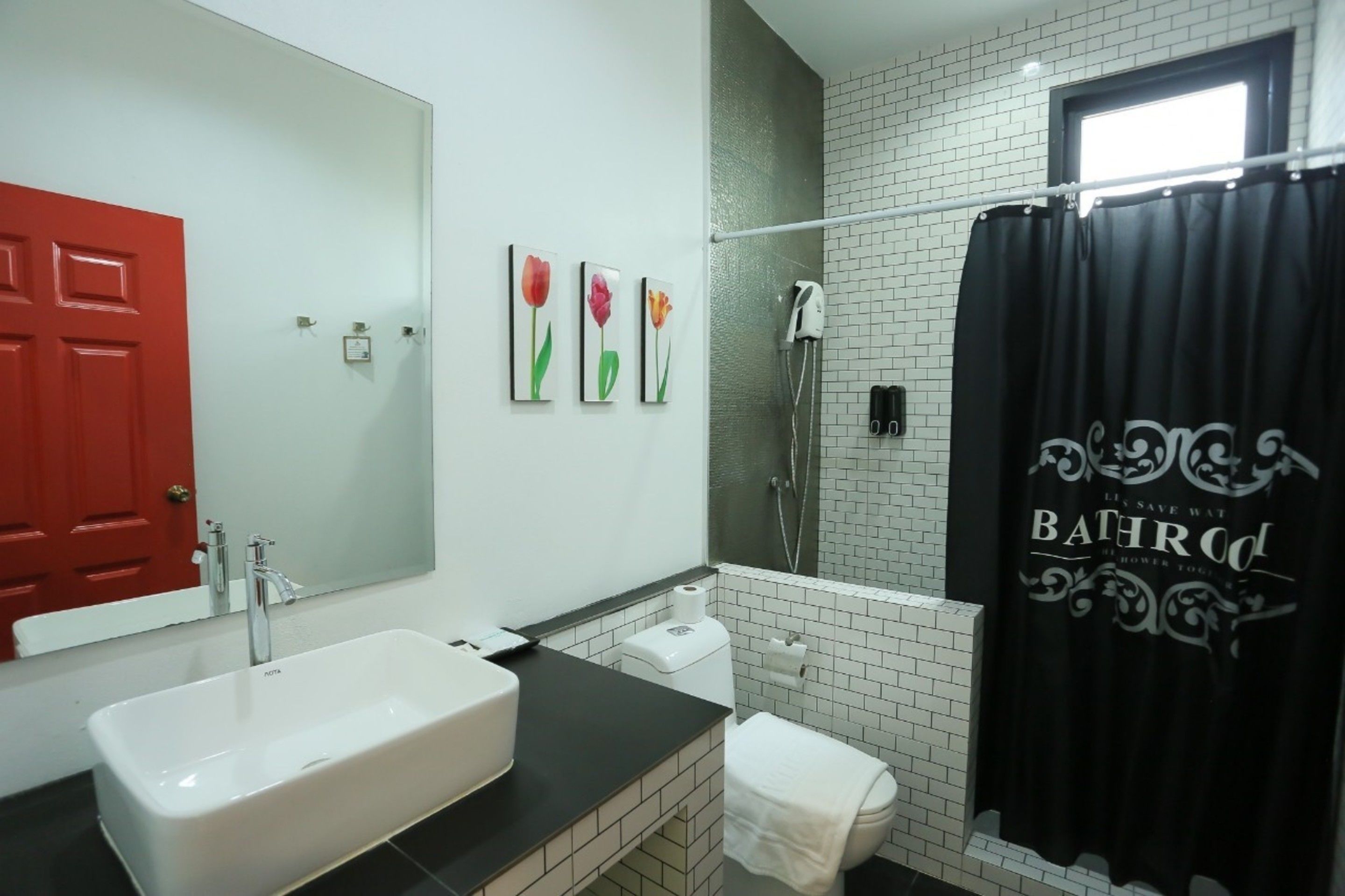 A bathroom with a white sink, a red door, a black shower curtain, and a white toilet.