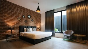 Un dormitorio moderno con pared de ladrillo, una cama grande, una lámpara colgante y vistas a través de una ventana con cortinas.