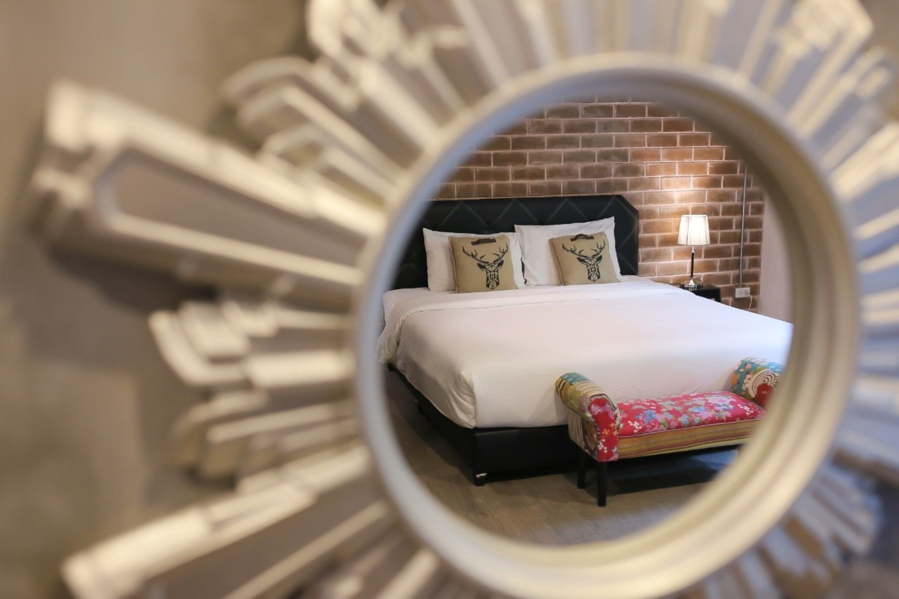 A bedroom with a brick wall, a bed with white bedding, and a nightstand with a lamp.