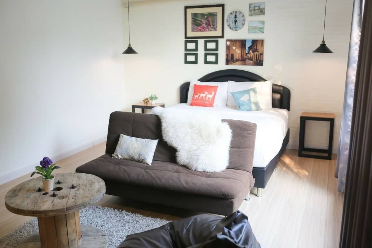 A modern bedroom with a bed, a brown sofa, a round wooden table, and a small potted plant.