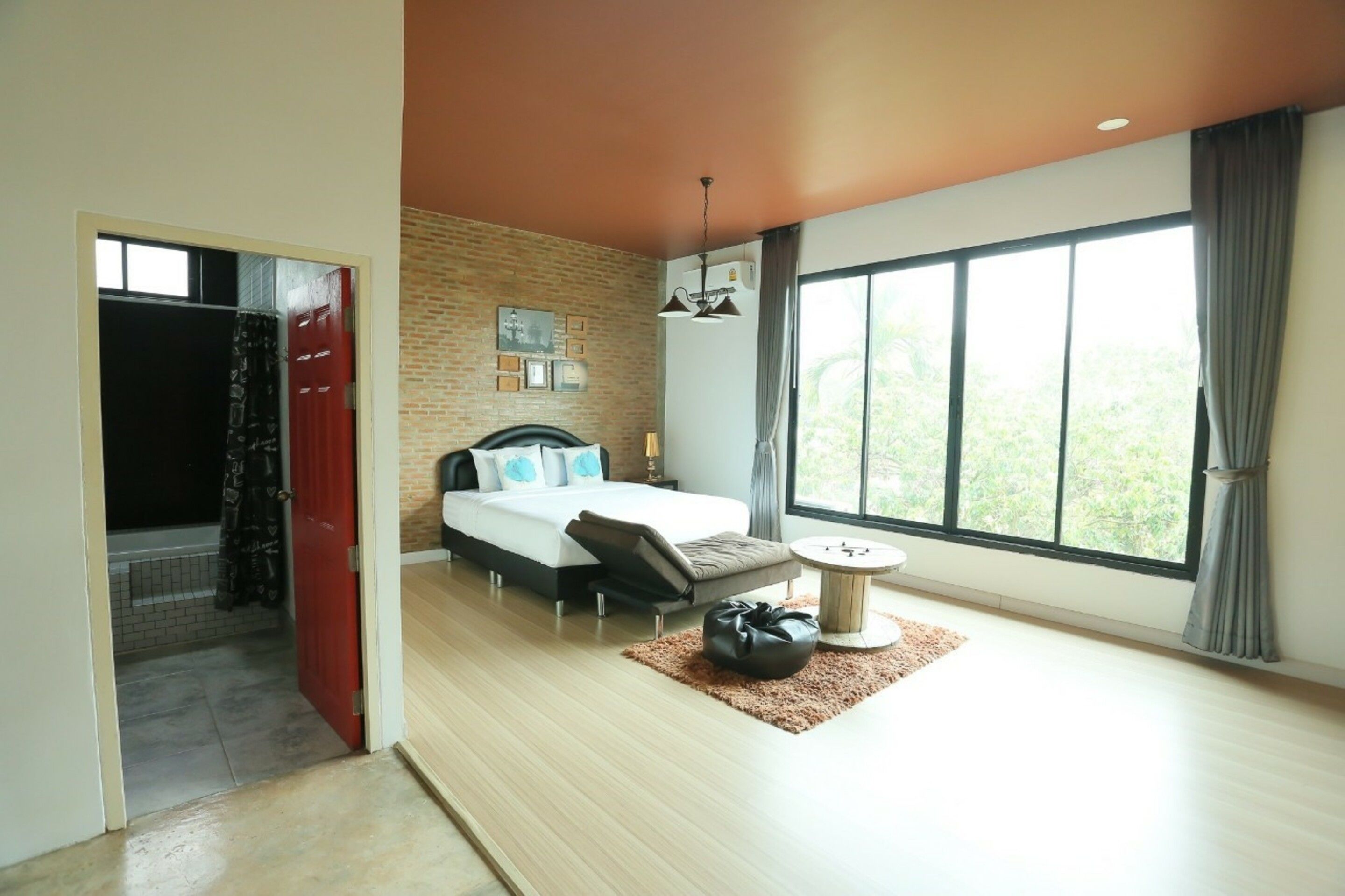 A modern bedroom with a large bed, a small round table, and a view of greenery through the window.