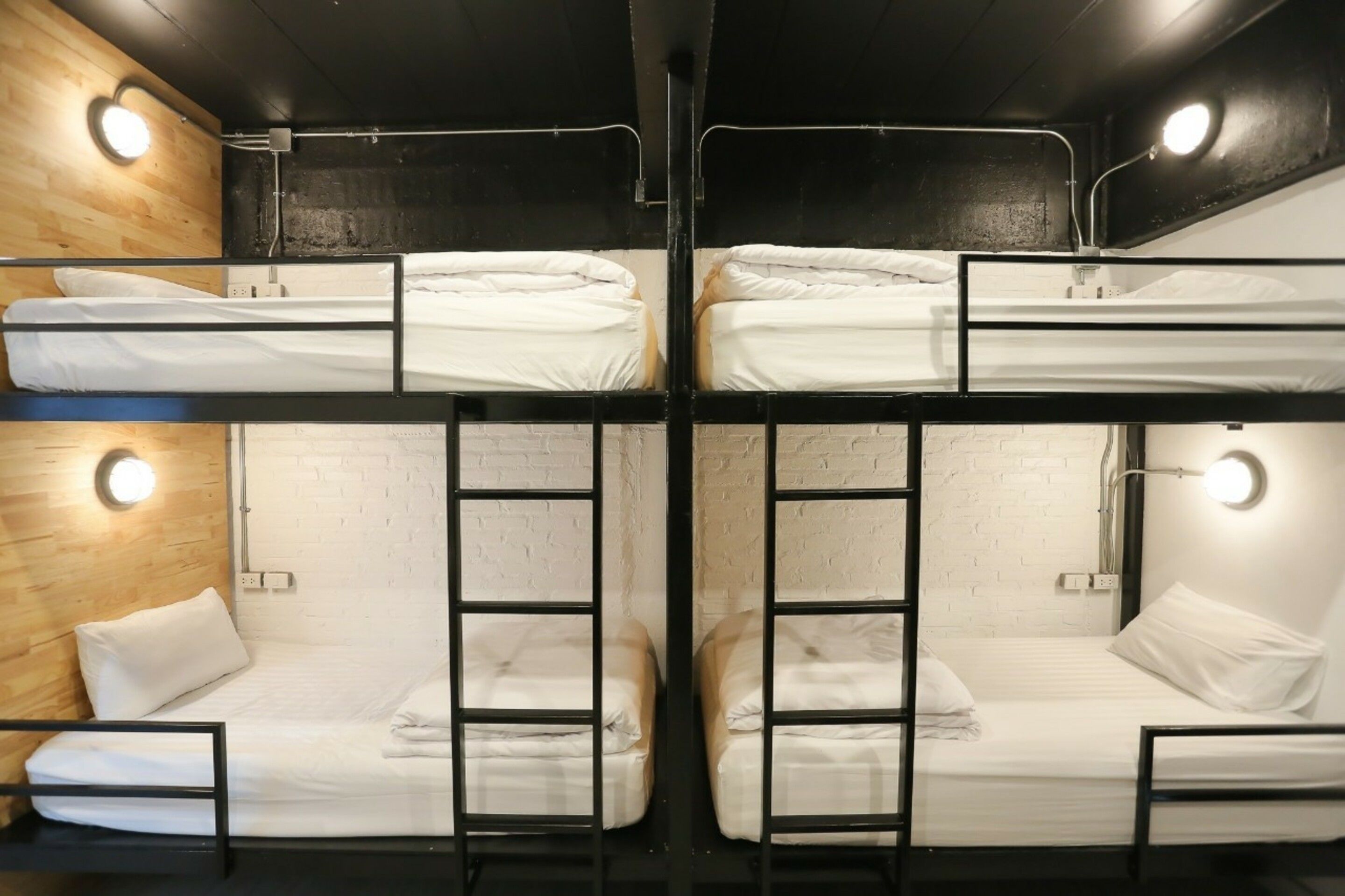 Habitación con literas, dos camas, cada una con almohada y manta. Dos luces fijadas en la pared y una escalera entre las camas.
