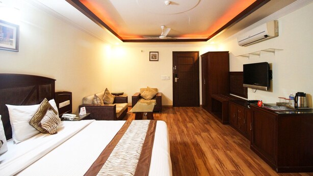 A hotel room with a bed, two sofas, a TV, a desk, and a ceiling fan. - Southview Apartment (New Delhi)