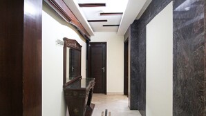 A hallway with a marble floor, a wooden cabinet with a glass top, and a dark door. - Southview Apartment (New Delhi)