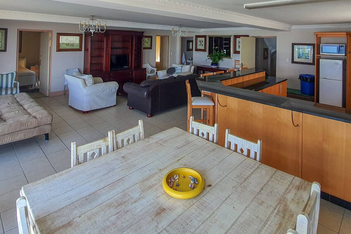 A spacious living area with a dining table, sofas, and a kitchen area with a microwave and refrigerator.