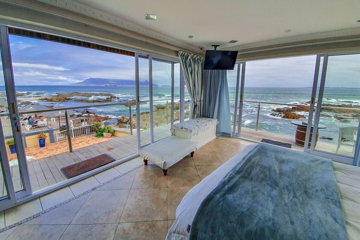 A balcony with a view of the ocean, a bed, and a TV.