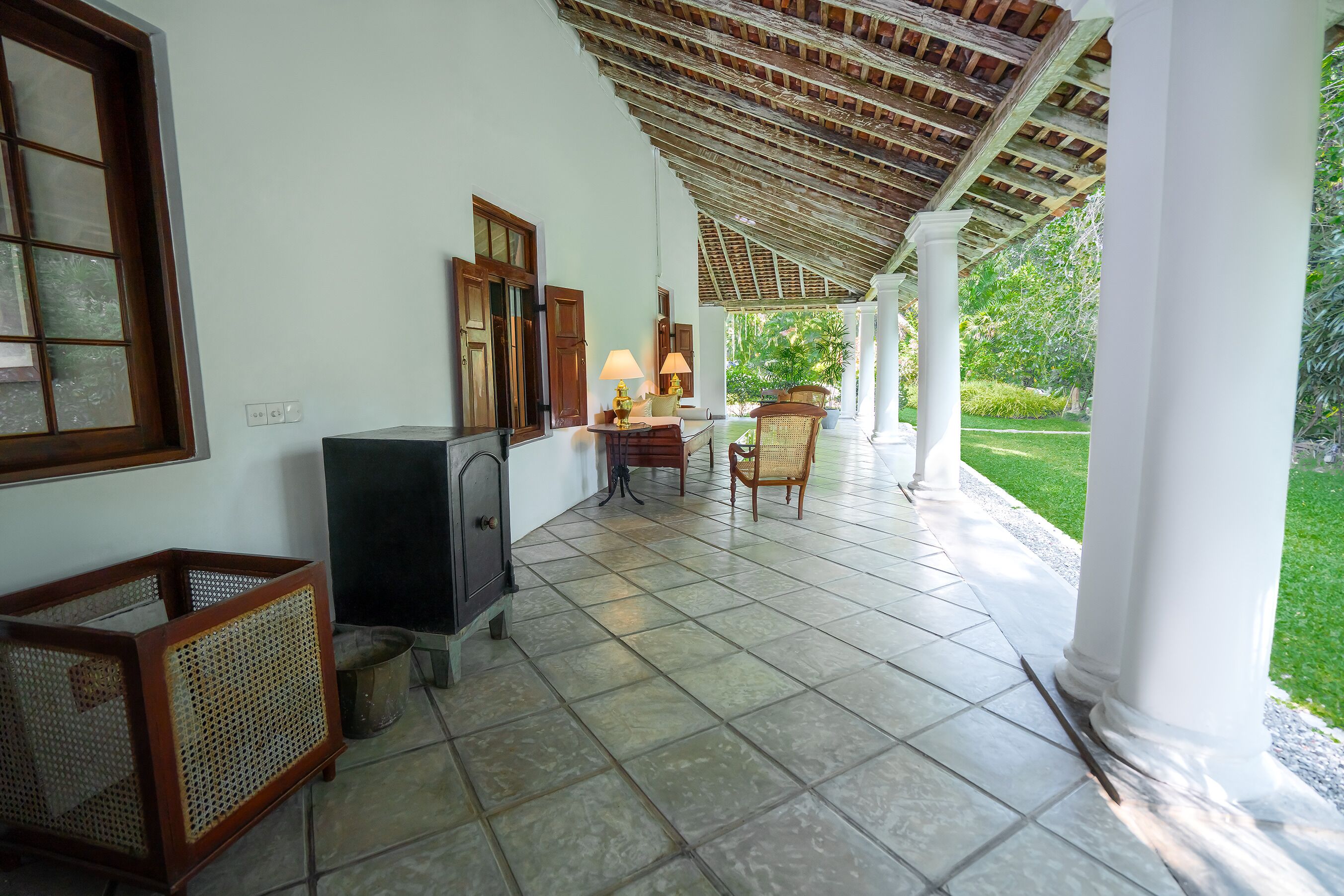 A covered outdoor area with tiled flooring, a fireplace, wicker furniture, and a view of greenery.