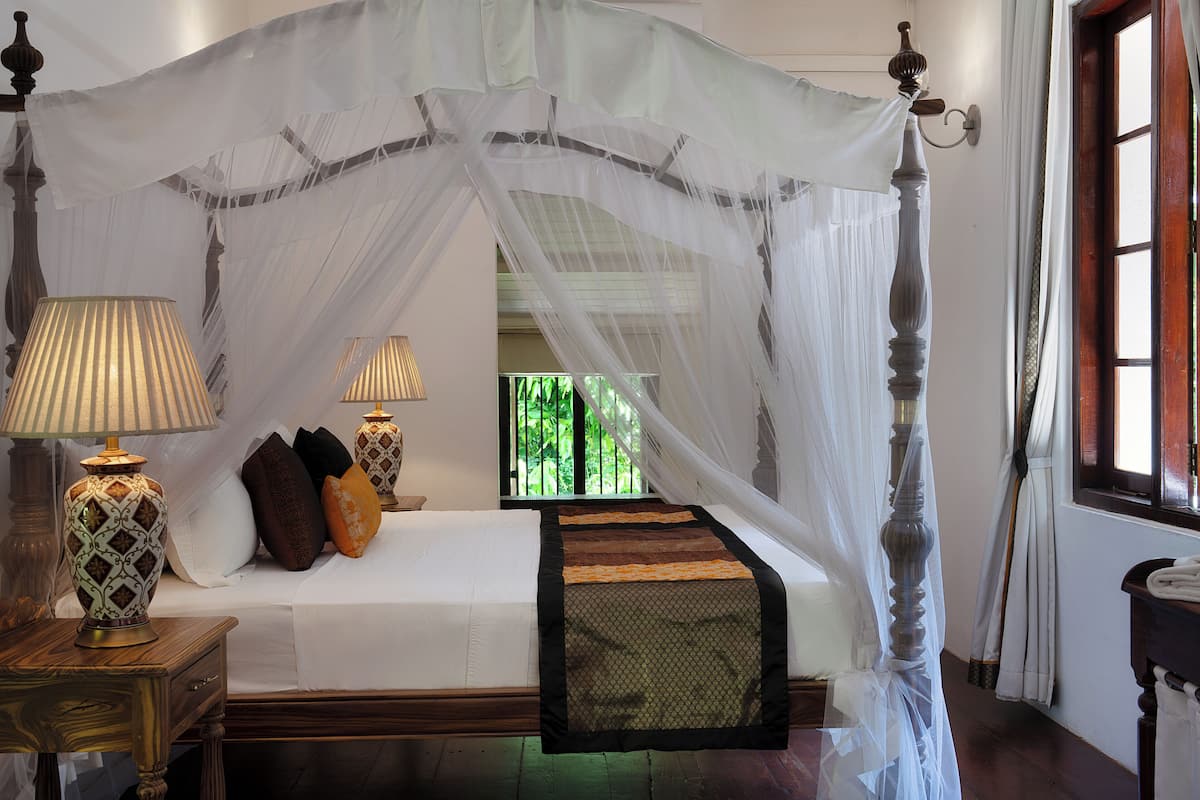 A four-poster bed with a canopy, bedside lamps, and a view of greenery outside.