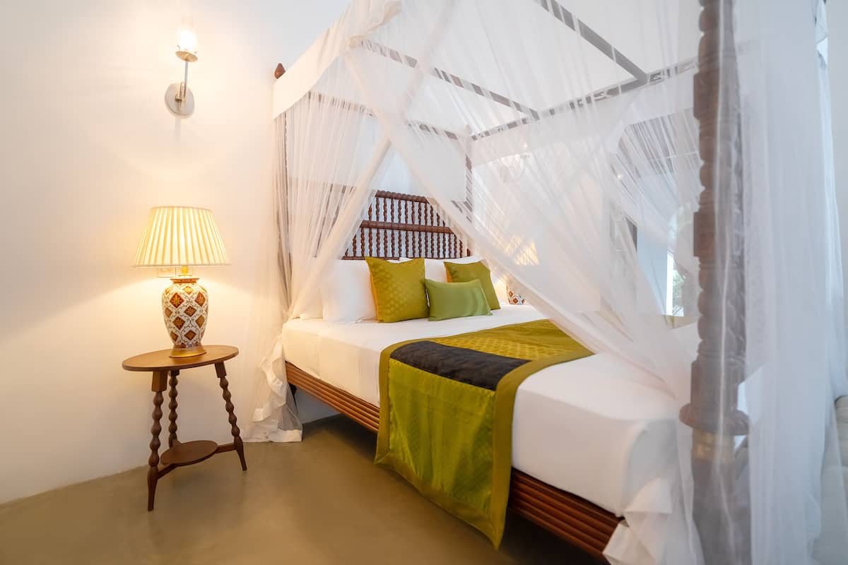 A bedroom with a canopy bed, a bedside lamp, and a small wooden table.