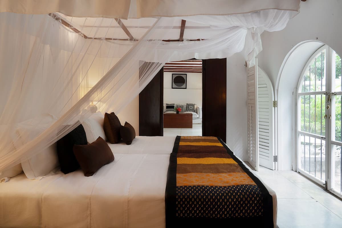 A bedroom with a canopy bed, a sofa, and a view of the outdoors.