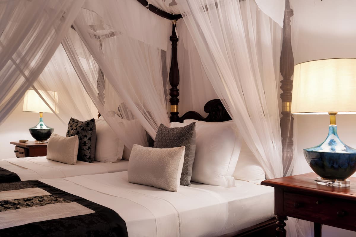 A bed with a canopy, multiple pillows, a bedside table with a lamp, and a nightstand with a lamp.