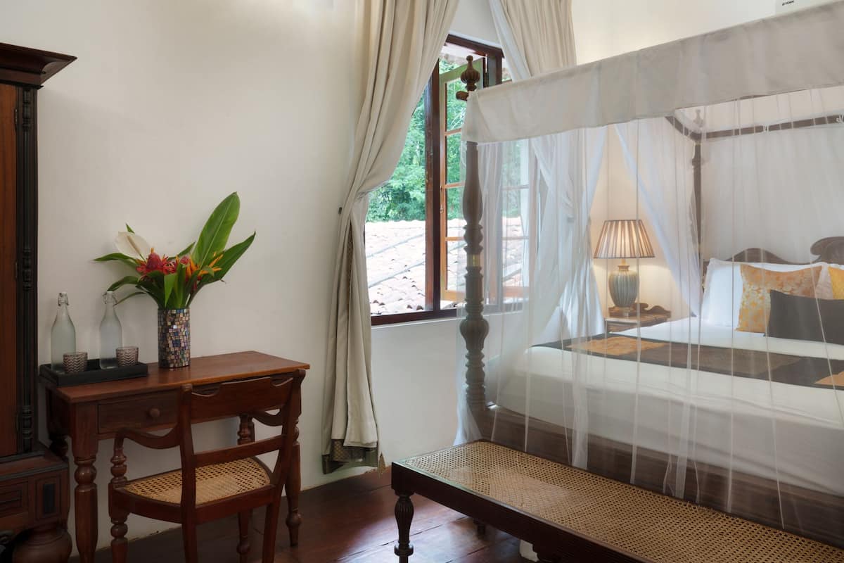 A room with a bed, a desk, a chair, a vase with flowers, and a window with curtains.