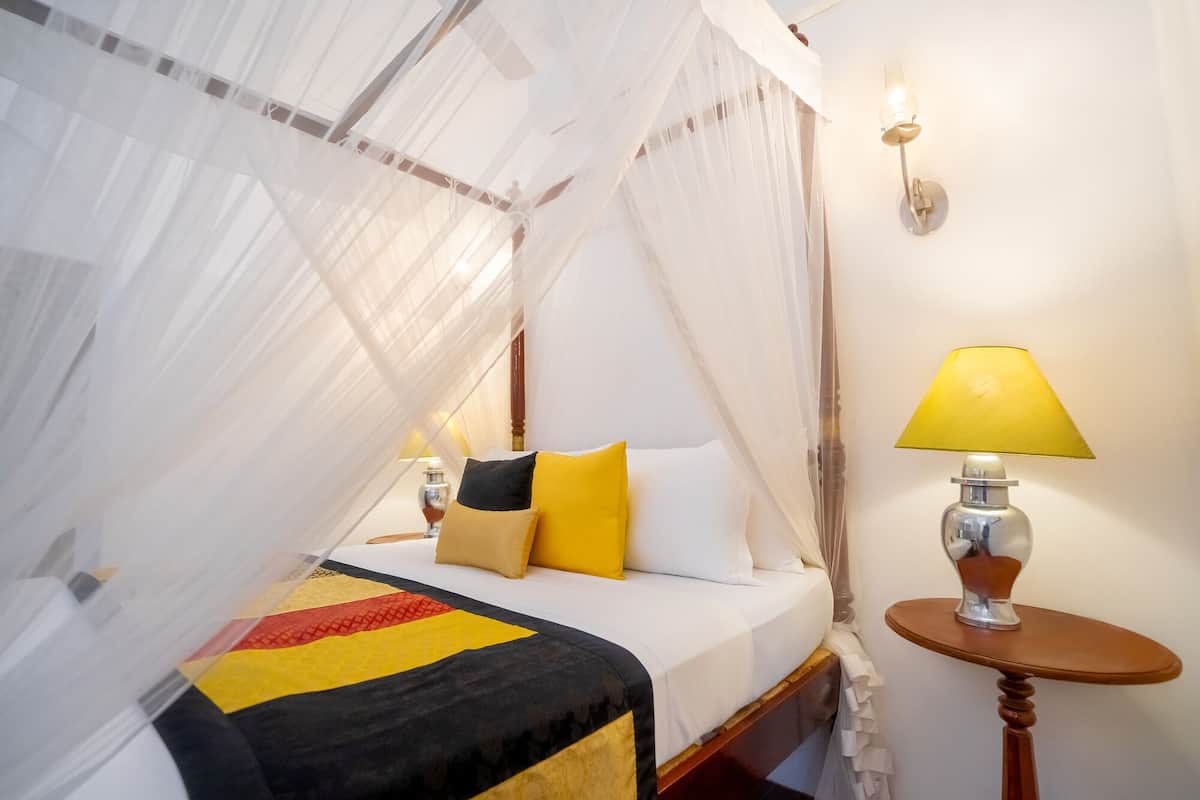 A bed with a canopy, bedside lamps, and a small table with a lamp.