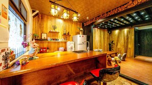A kitchen with wooden walls, a wooden countertop, and a refrigerator. There are two bar stools with red seats. - Cat Lazy B&B (Luodong)