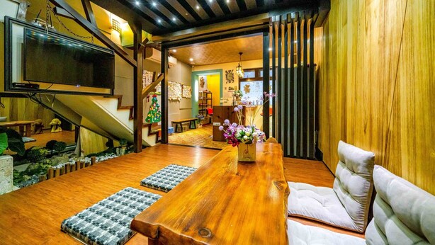 A spacious living room with a wooden dining table, cushioned seating, a television mounted on the wall, and a staircase leading to another level. - Cat Lazy B&B (Luodong)