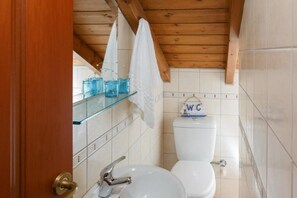 Un baño con techo de madera, azulejos blancos, un lavabo blanco y un inodoro con el letrero 'WC'.