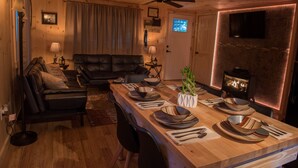 A cozy living room with a wooden ceiling, a fireplace, and a dining area set with plates and cutlery.