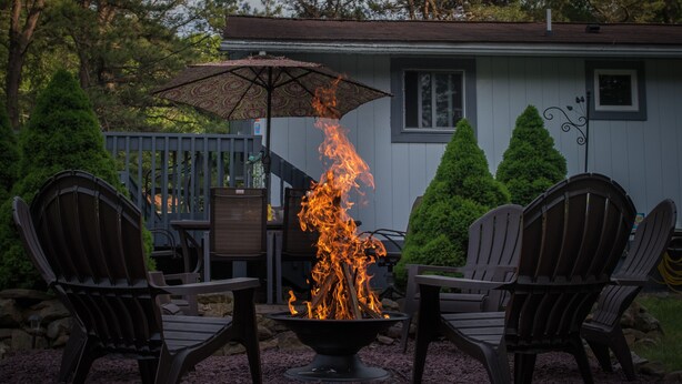 A fire pit with chairs around it, a patio umbrella, and a house in the background.