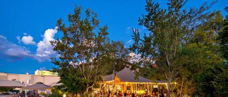 Un espacio para eventos al aire libre con zona de estar cubierta, rodeado de árboles y vegetación.