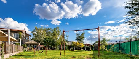 A backyard with a swing set, a covered seating area, and a fenced yard.