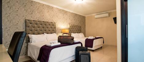 A hotel room with two beds, a desk, and a chair. There is a suitcase and a handbag on the bed.