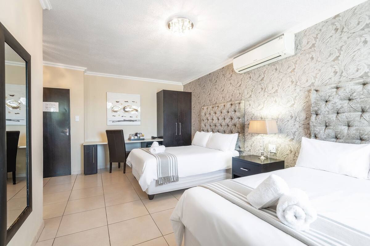 Habitación de hotel con dos camas, un escritorio, una silla y un espejo grande.