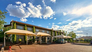 A hotel with a brick facade, outdoor seating with umbrellas, and a parking area.