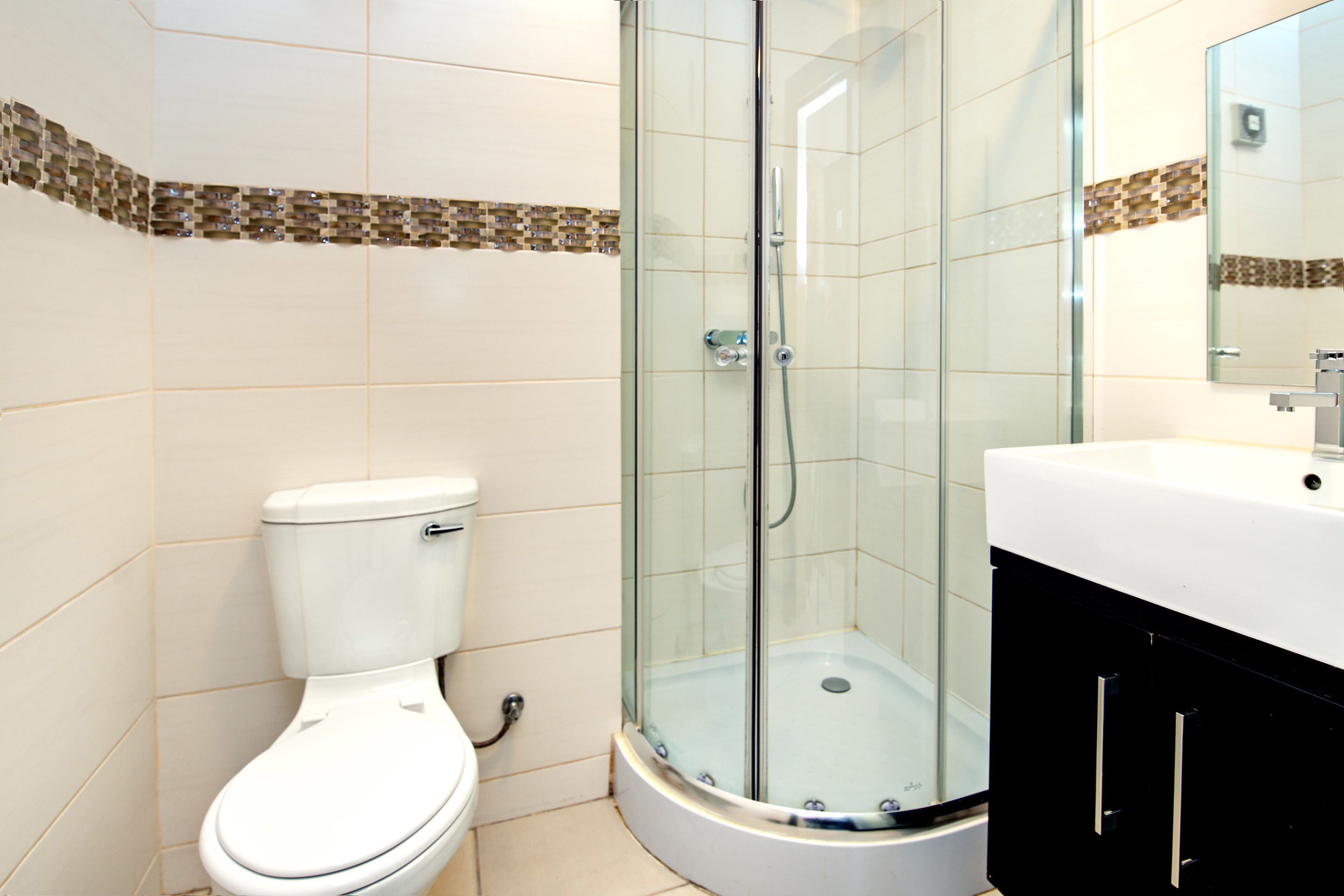 A bathroom with a toilet, a glass-enclosed shower, and a sink with a mirror.