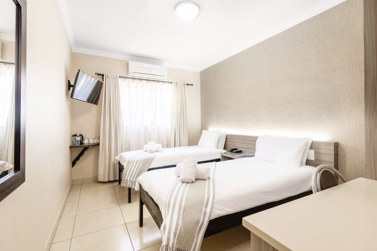 Habitación de hotel con dos camas, un televisor montado en la pared, una mesita y una ventana con cortinas.