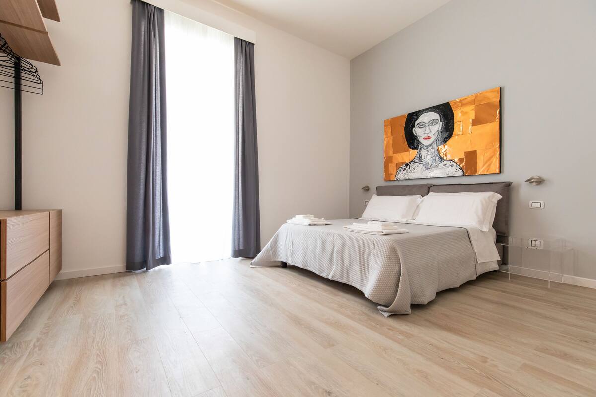 Een moderne slaapkamer met een bed, een dressoir en een schilderij aan de muur.