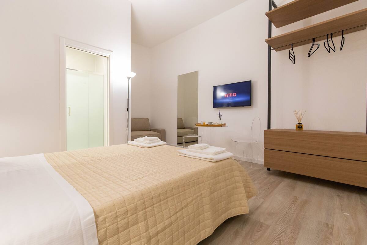 Een moderne hotelkamer met een bed, een aan de muur bevestigde televisie, een houten dressoir en een spiegel.