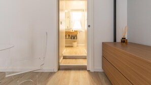 Een gang die leidt naar een badkamer met een houten vloer en een witte muur.