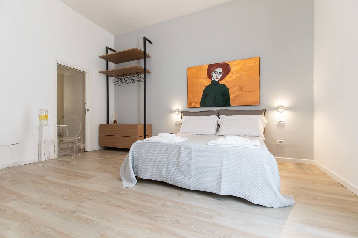 Een moderne slaapkamer met een bed, een schilderij en een bureau met stoel.