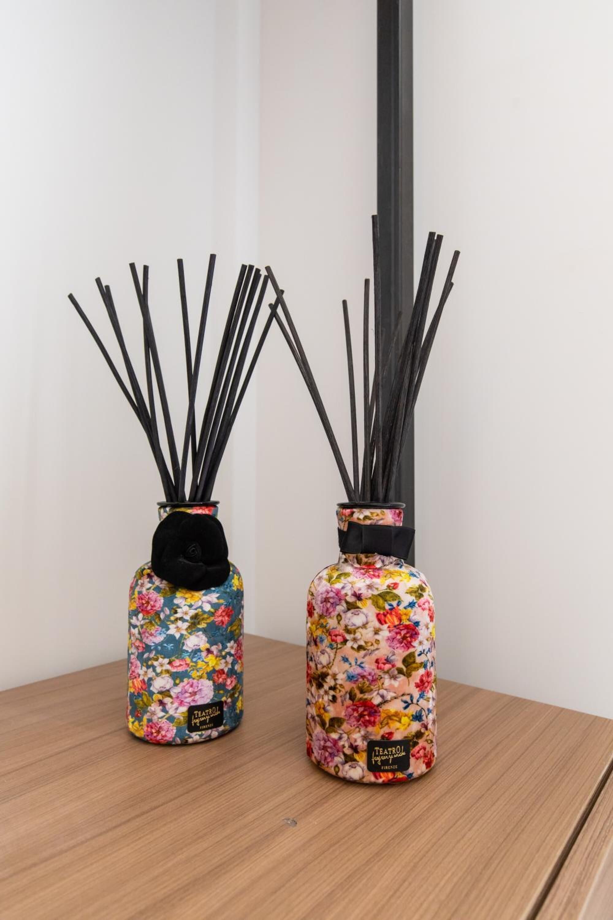 Two vases with floral patterns and reed diffusers on a wooden table.