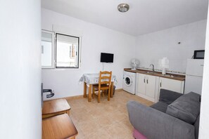 Une cuisine compacte comprenant un lave-linge, une table à manger avec des chaises, un canapé et un téléviseur.